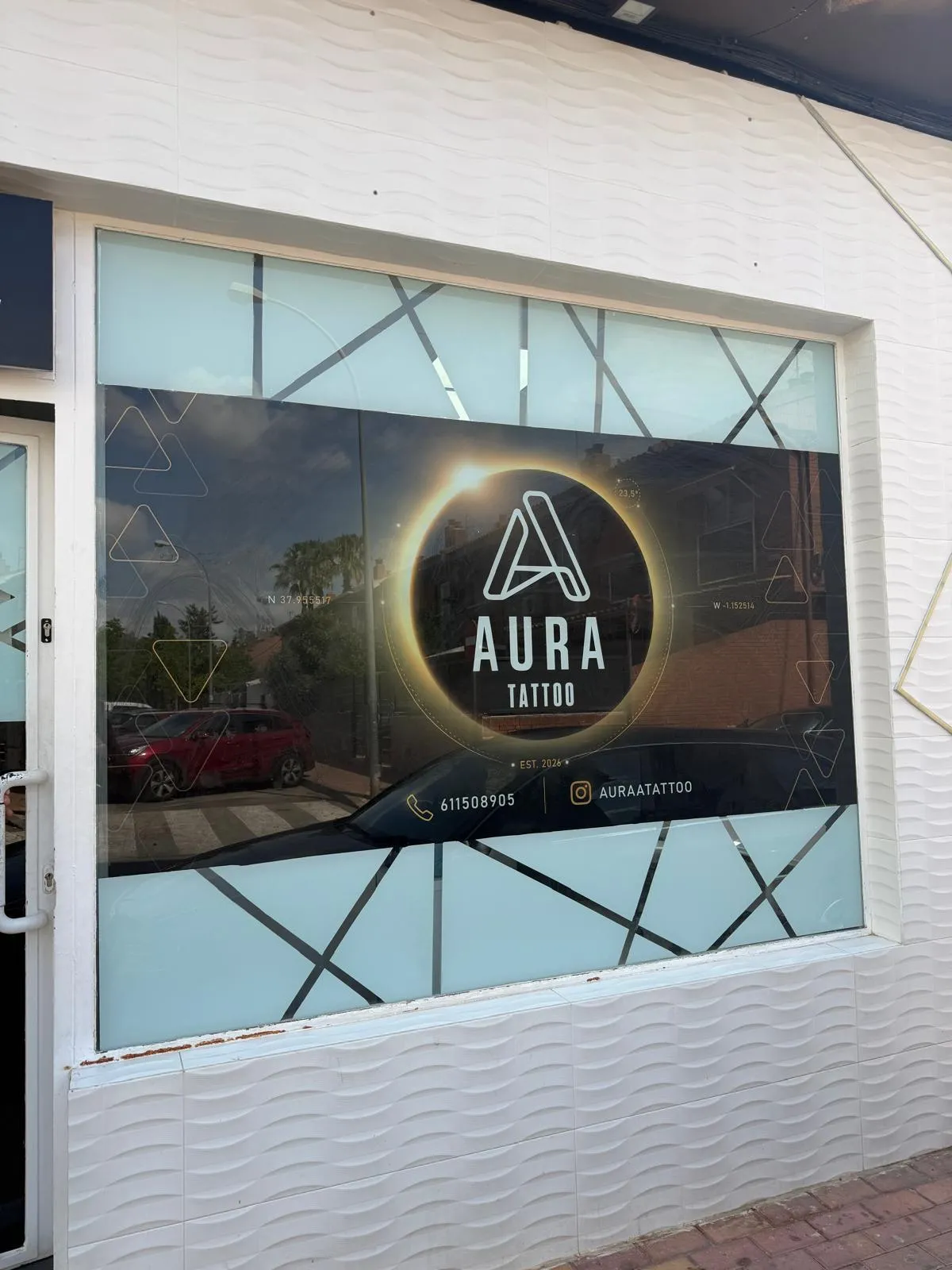 Escaparate del estudio Aura Tattoo con vinilo impreso oscuro, logotipo de eclipse y datos de contacto