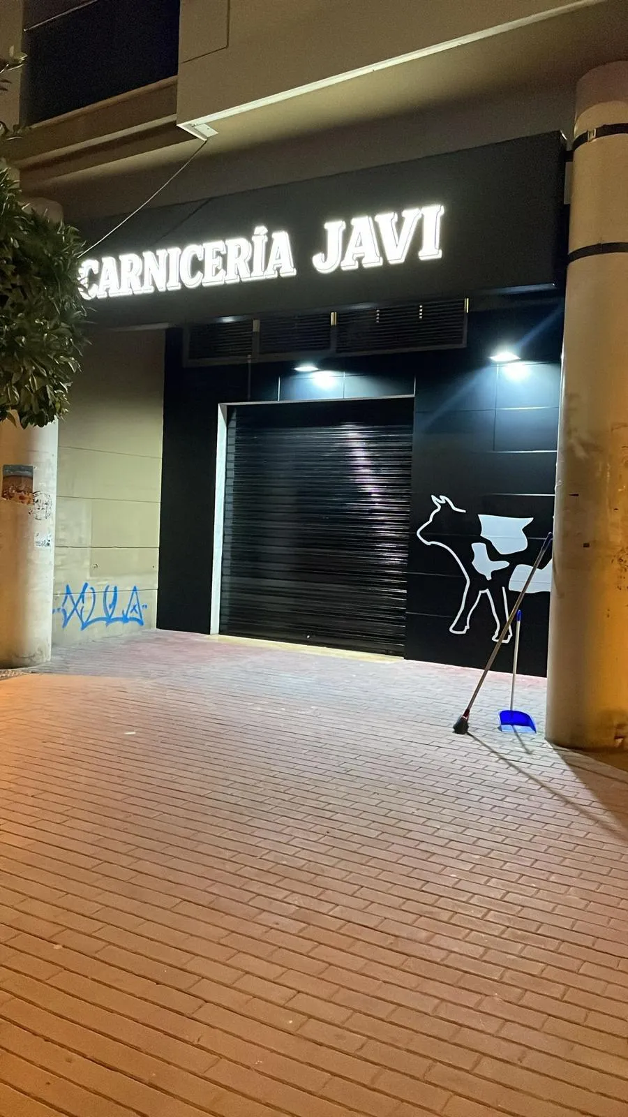 Fachada de la Carnicería Javi de noche con luminoso frontal de lona impresa retroiluminada y silueta de vaca en vinilo sobre panel negro
